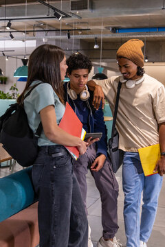 Diverse students in study lounge, viewing tablet, holding red and yellow folders with headphones