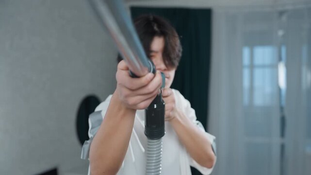Youthful individual mimicking firearm with cheerful attitude in home setting. Young boy engaging in playful pretend shooting with vacuum cleaner as rifle in humorous domestic moment