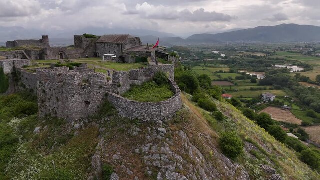 4K drone tracking flyby of Rozafa Castle with 180 degree yaw focusing on Albanian flag over stone ramparts, Shkoder