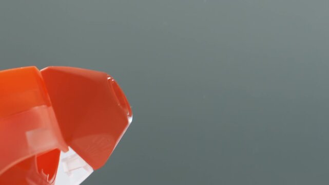 Closeup orange spray nozzle emitting mist, studio shot showing fine atomized droplets and sleek plastic bottle, slowmotion trigger press, neutral grey background, product detail for cleaning demo