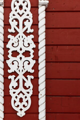 Obraz premium Carved white wooden trim with ornate scrollwork flanked by twisted columns on a red painted wooden wall, offering rustic, traditional architectural detail and vintage charm for Russian exterior design