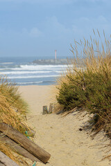 Obraz premium Sandy path leading through dunes to the ocean with a lighthouse in the background The Concept of journey and hope