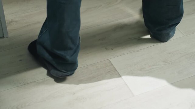 Gentle steps across smooth laminate flooring surface. Close view of socked feet taking slow pace indoors. Focused image of textured laminate floor with shadow and scuff details during quiet moment