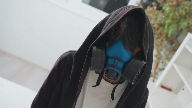 Person sanitizing room quietly. Individual in protective gear disinfects space calmly. Hooded figure with respirator carefully disinfects peaceful interior surrounding window and shelves