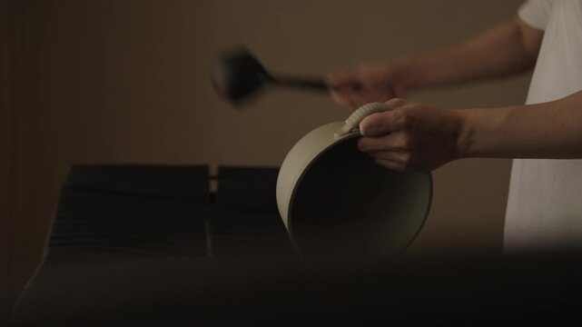 Cropped shot of sound engineer striking large pan with ladle to demonstrate sound absorbing properties of acoustic foam panels, concept of soundproofing technology and noise reduction materials.