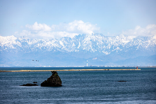 雨晴海岸の青い海原の向こうに、冠雪した雄大な立山連峰がそびえ立つ絶景