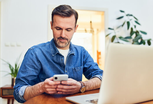 Man using smartphone at desk with laptop in home office