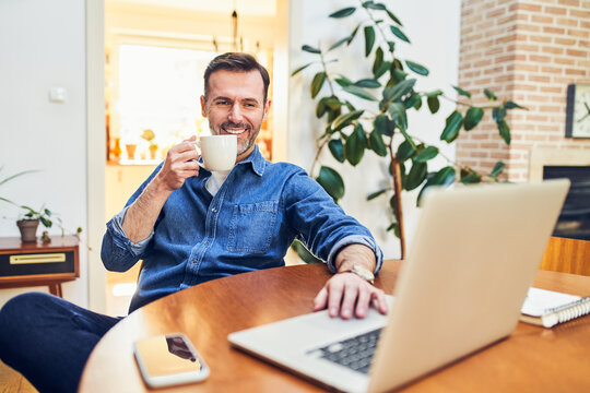 Man drinking coffee while working on laptop at home