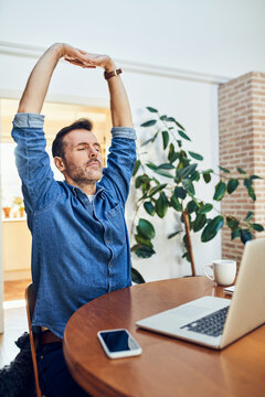 Man stretching arms at desk during work break at home