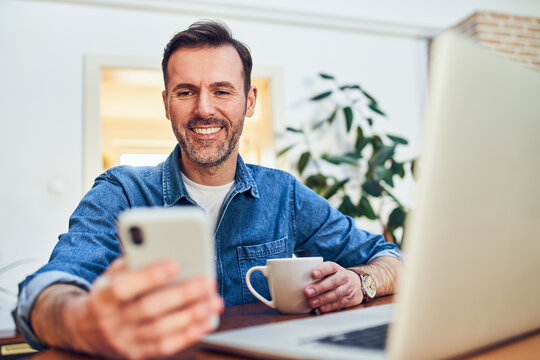 Man smiling with smartphone and coffee at home desk