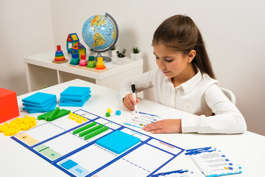 A young girl explores the relationship between units, tens, and hundreds using a professional math kit and a place value mat in a homeschool setting.