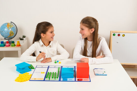 Two young students sitting at a desk, smiling and collaborating on a math lesson using colorful base ten blocks to understand place values from ones to thousands.