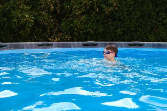 Caucasian boy spends time playing in backyard pool. Child learning to swim in swimming goggles having summer fun, outdoor leisure, active lifestyle. Summertime pleasure. Enjoy moment. Aquatic safety.