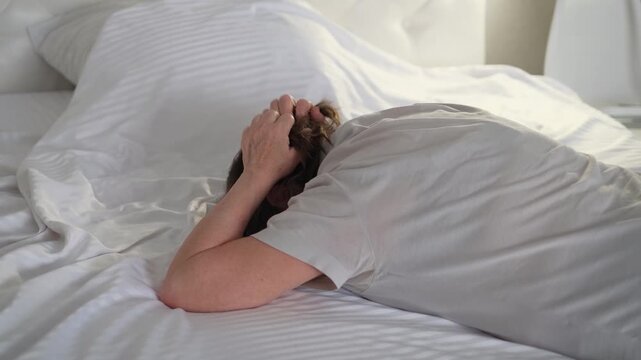 An elderly woman cries hysterically on her bed, clutching her hair