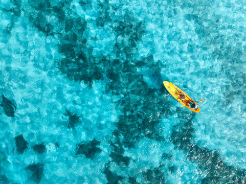Aerial drone view of a kayakers paddling through vibrant turquoise water in deep blue sea in summer. Mallorca, Spain. Balearic Islands. Tropical paradise. Top down view of canoe. Outdoor adventure