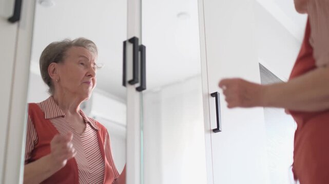 A cheerful, well-groomed old woman dances and sings while looking in the mirror