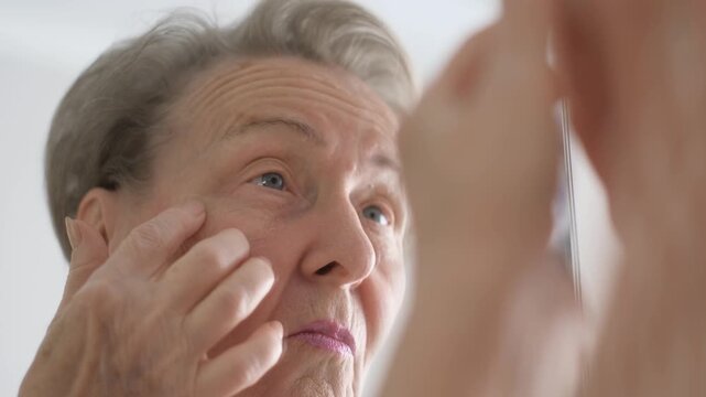 Senior woman assessing the condition of the skin around her eyes while looking in the mirror, close-up