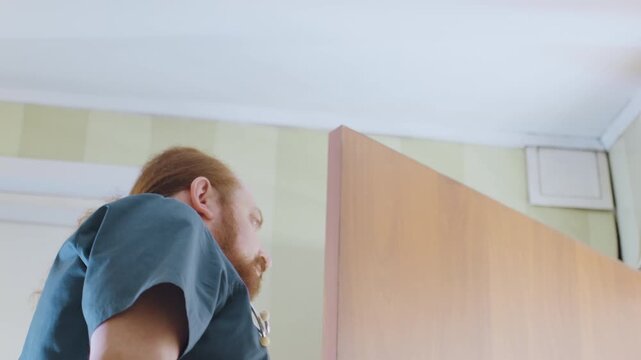 White paramedic entering home hallway, red hair medic in teal scrubs opens door with cautious look, low angle view reveals wallpapered interior and ceiling, quiet tense atmosphere during urgent