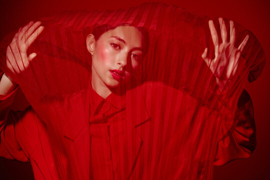 Stylish woman in red outfit stands behind vibrant red fabric, creating abstract patterns. Concept of high fashion, creativity, and beauty editorial with dramatic lighting.