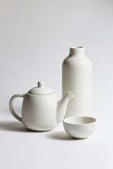 Fototapeta premium White ceramic teapot, bottle, and bowl arranged on a light background showcasing minimalist design and smooth surfaces for modern tableware aesthetics