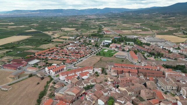 A drone view of a rural town with red-roofed houses, open fields and surrounding hills in Camino de Santiago, Navarrete, Spain