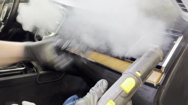 Dry cleaning of the car leather interior, car door trim using a special brush. The detailing master cleans the car interior with a hot steam cleaner, brush, microfiber. Concept of car interior care.