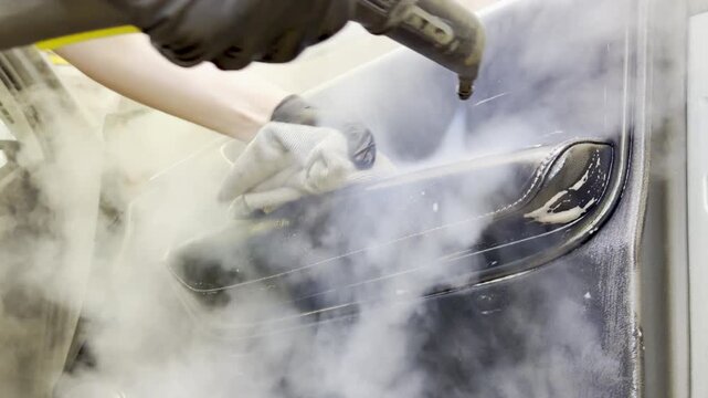 Dry cleaning of the car leather interior, car door trim using a special brush. The detailing master cleans the car interior with a hot steam cleaner, brush, microfiber. Concept of car interior care.