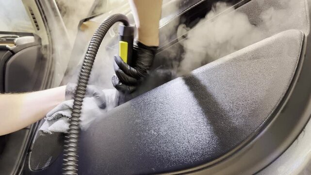 Dry cleaning of the car leather interior, car door trim using a special brush. The detailing master cleans the car interior with a hot steam cleaner, brush, microfiber. Concept of car interior care.