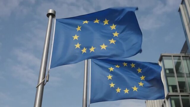 European union flags waving in front of a modern glass office building