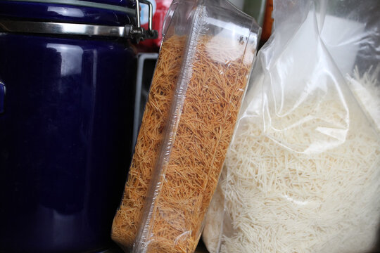 Roasted golden and raw white shredded kataifi fillo (phyllo) dough next to a blue ceramic storage canister in a kitchen pantry. Ingredient for desserts or savory dishes.