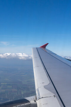 Airplane wing with red winglet flying over green fields