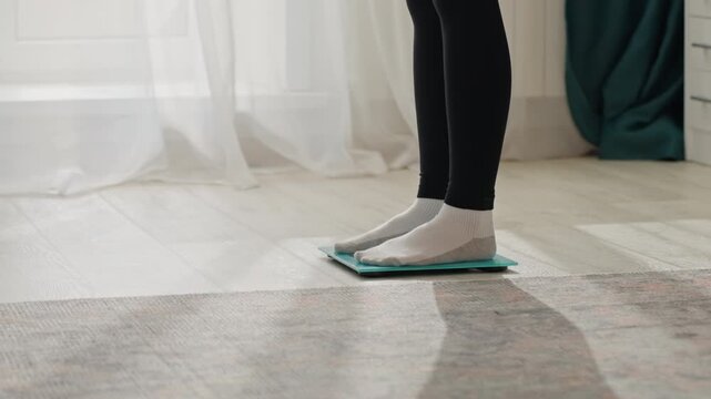 Home bedroom sockson feet testing scale. Soft morning light through sheer curtains, teal glass scale on rug, socksclad feet step tentatively onto digital display minimal interior, calm mood, focus