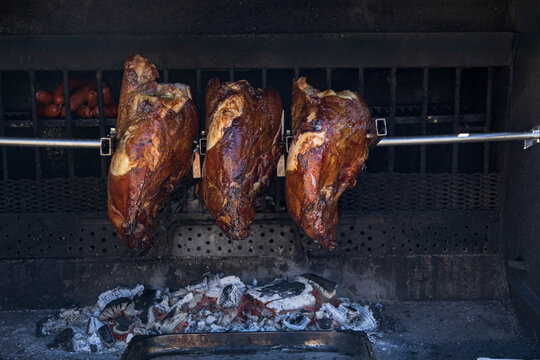 Roasting pork ham or knee on a spit over an open fire or coals. It has an even roast, a crispy crust and remains juicy inside. Concept of a popular street food with copy space.