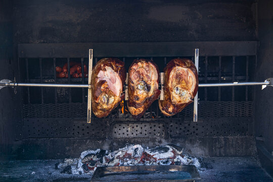 Hot pork ham on a spit over an open fire or coals close-up on a black background.The meat is slowly rotated on a metal skewer using an electric drive. Concept of a popular street food with copy space.