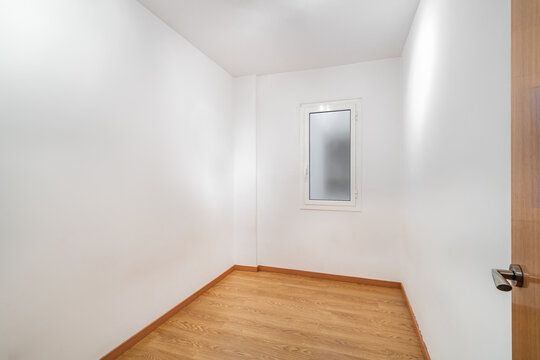 Empty room with white walls and wooden floor. A small window allows natural light to enter. The space is minimalistic and uncluttered.