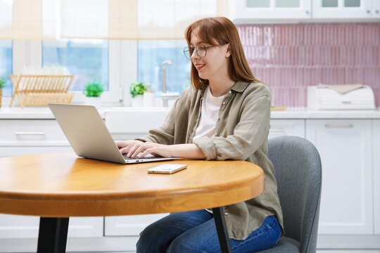 Woman working with laptop at wooden table in kitchen