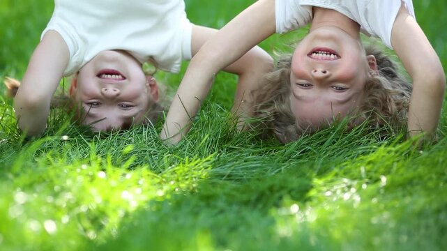 Funny kids do a handstand in a summer park on green grass. Slow motion