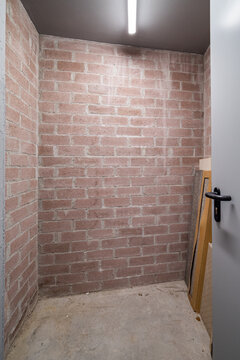 Empty storage room with exposed brick walls and concrete floor. A door is partially open, revealing a simple, minimalistic space