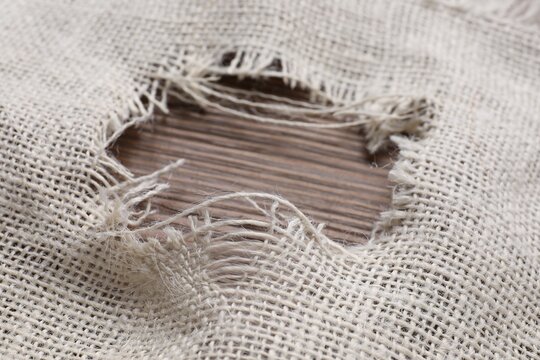 Burlap fabric with torn hole on wooden table, closeup
