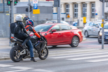 Fototapeta premium Couple on a motorcycle waits at an intersection. A rider and passenger in helmets wait for light.