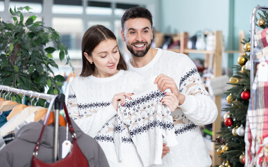 Obraz premium Married couple choose sweaters against background of Christmas tree in a clothing store