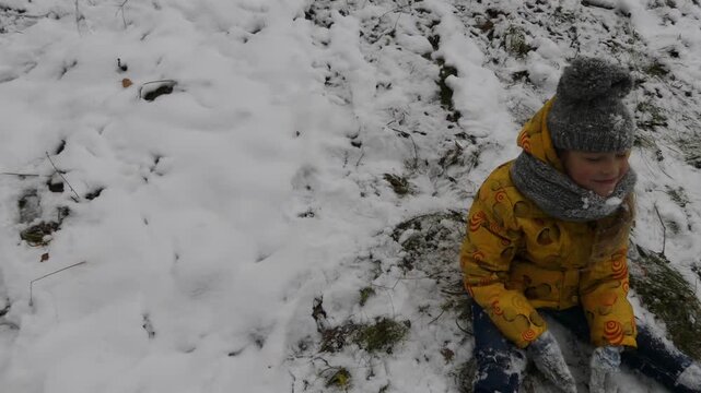 Little girl sits in snow in winter city park.