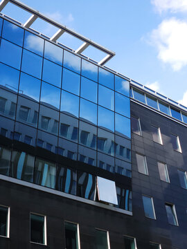 Modern glass office building reflects sky and clouds on its facade with rows of windows