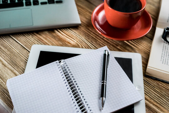 Modern cozy workspace setup with laptop, red coffee cup, open textbook and stationery on wooden background