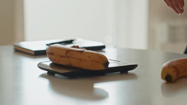 Bananas on sleek digital scale, hands arranging bunch beside notebook, soft natural light and gentle shadows, serene modern countertop, influencer style recipe prep, focus on portion control