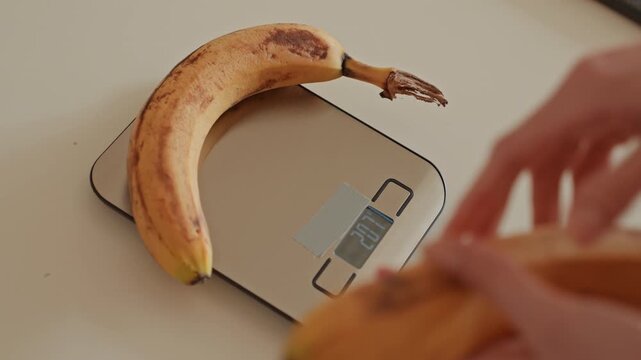 Overripe bananas on digital scale, home cook measures fruit for baking and compost, closeup hands placing bunch on sleek stainless platform, neutral countertop, warm natural light, mindful sustainable