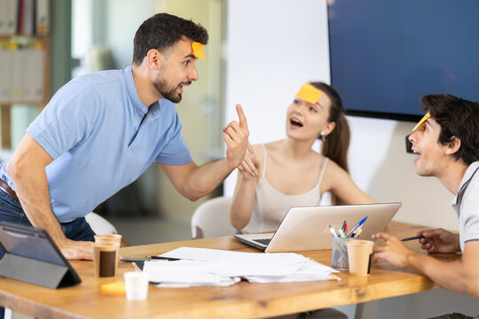 Focused young colleagues trying to guess names on forehead while spending leisure moments in office