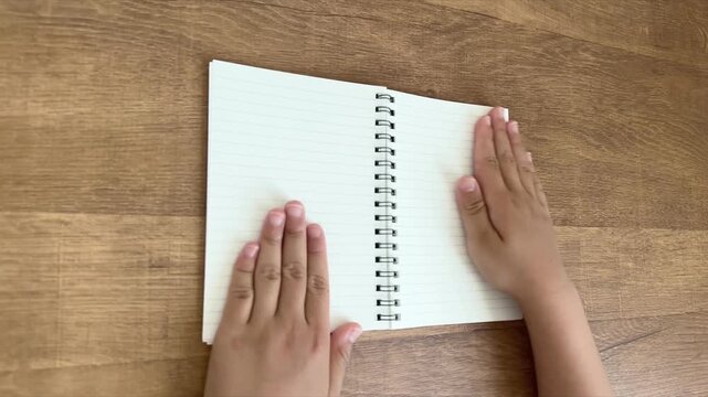 Child Hands Smoothing an Open Spiral Notebook from an Angled Overhead View, 4K Slow Motion Silent Video