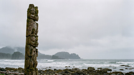 Obraz premium Ancient carved totem pole stands sentinel on a rugged Canadian coastline, a powerful cultural symbol against the dramatic misty landscapes