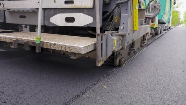 Asphalt paving machine lays fresh asphalt on road surface, showcasing continuous action of road construction process in urban setting